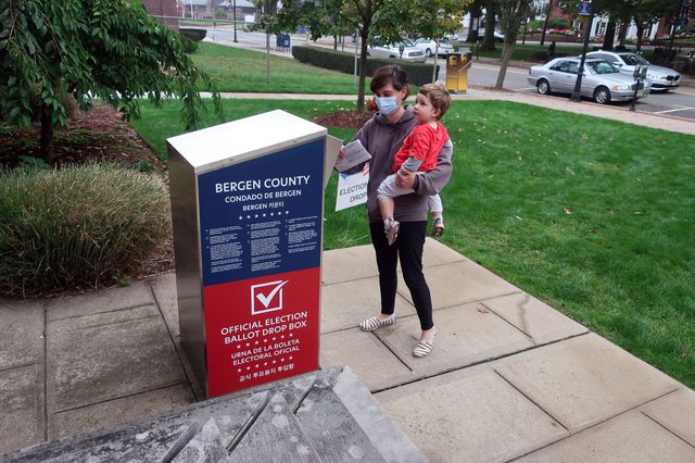 Woman in a face mask carrying a child drops a ballot in a drop box in Rutherford, New Jersey